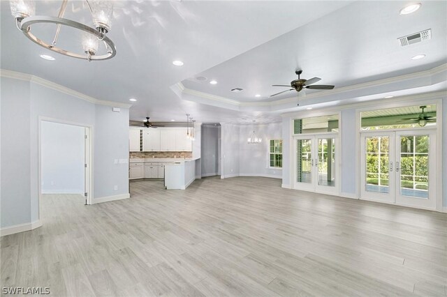 unfurnished living room with a raised ceiling, french doors, ceiling fan with notable chandelier, and ornamental molding