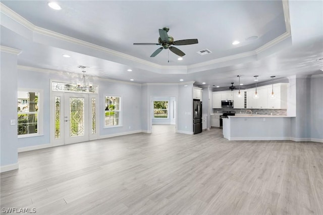 unfurnished living room featuring ceiling fan with notable chandelier, crown molding, light hardwood / wood-style flooring, and a tray ceiling