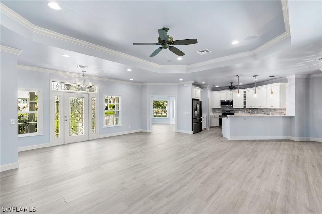 unfurnished living room with light hardwood / wood-style flooring, a tray ceiling, ceiling fan with notable chandelier, and ornamental molding