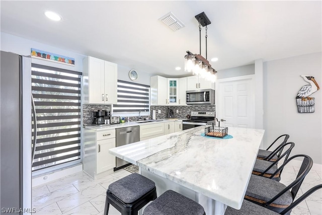 kitchen with white cabinetry, light stone counters, decorative light fixtures, a center island, and appliances with stainless steel finishes