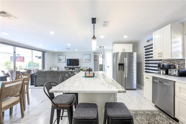 kitchen featuring pendant lighting, white cabinetry, stainless steel appliances, light stone countertops, and decorative backsplash