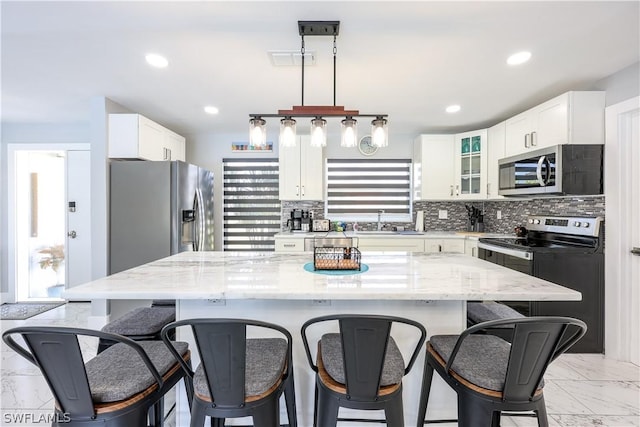 kitchen featuring a kitchen island, white cabinetry, hanging light fixtures, stainless steel appliances, and light stone countertops