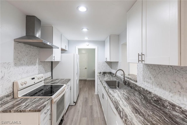 kitchen with sink, white appliances, white cabinetry, wall chimney exhaust hood, and light wood-type flooring