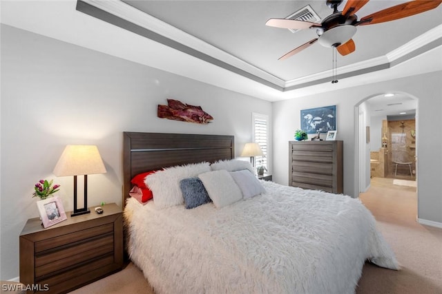 carpeted bedroom featuring ceiling fan, a raised ceiling, ornamental molding, and ensuite bathroom