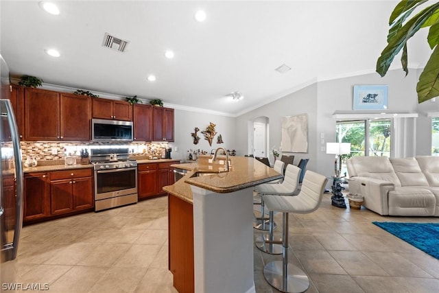 kitchen with light stone countertops, appliances with stainless steel finishes, a kitchen breakfast bar, ornamental molding, and a center island with sink