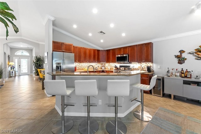 kitchen with appliances with stainless steel finishes, vaulted ceiling, ornamental molding, and a breakfast bar area