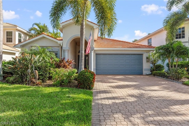 mediterranean / spanish home featuring a tiled roof, decorative driveway, an attached garage, stucco siding, and a front lawn