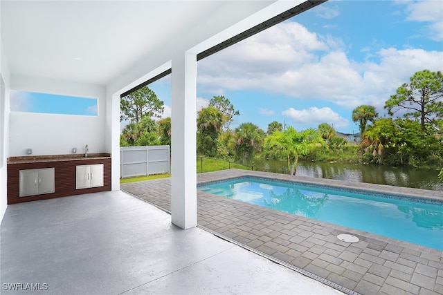 view of pool with a patio, sink, and a water view