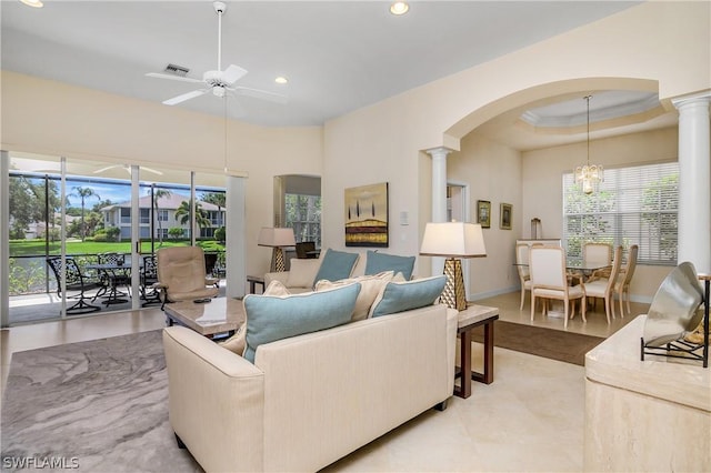 tiled living room featuring ceiling fan, a healthy amount of sunlight, a raised ceiling, and decorative columns