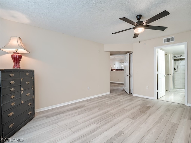 unfurnished bedroom with a textured ceiling, light wood-type flooring, ensuite bath, and ceiling fan