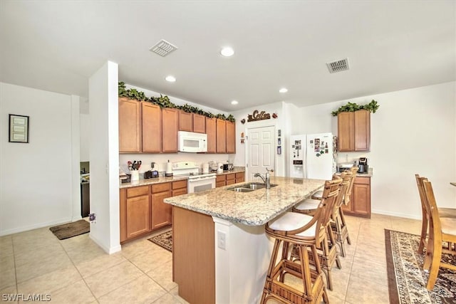 kitchen with light tile patterned flooring, white appliances, sink, and an island with sink