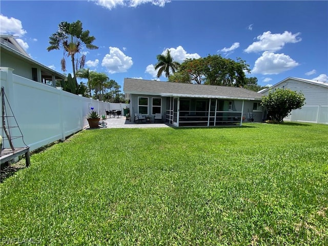 rear view of property featuring a lawn, a sunroom, and a patio