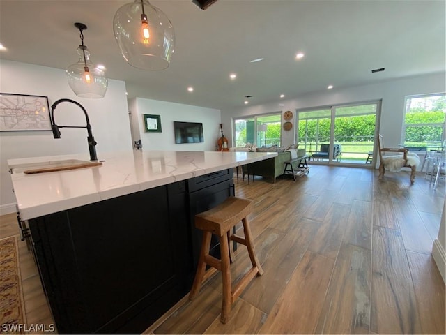 kitchen with light stone countertops, a large island, decorative light fixtures, and hardwood / wood-style flooring