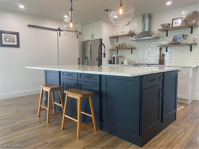 kitchen with backsplash, wall chimney exhaust hood, stainless steel fridge, a barn door, and white cabinetry