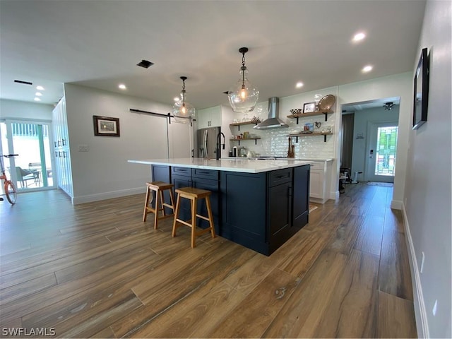 kitchen with white cabinetry, wall chimney exhaust hood, stainless steel fridge, decorative light fixtures, and decorative backsplash