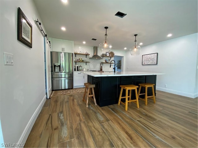 kitchen with white cabinets, a spacious island, wall chimney range hood, stainless steel refrigerator with ice dispenser, and a barn door