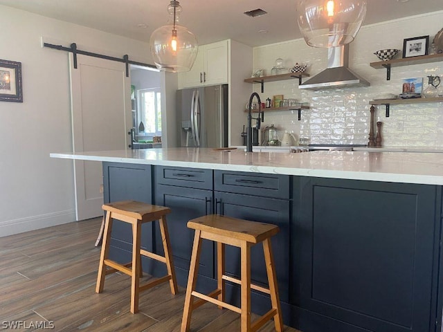 kitchen with stainless steel fridge with ice dispenser, a barn door, blue cabinets, and hardwood / wood-style floors