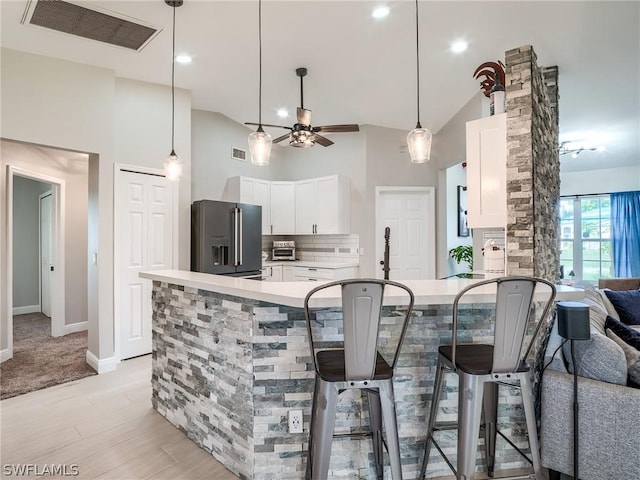 kitchen featuring a breakfast bar area, backsplash, high vaulted ceiling, high end black fridge, and white cabinets