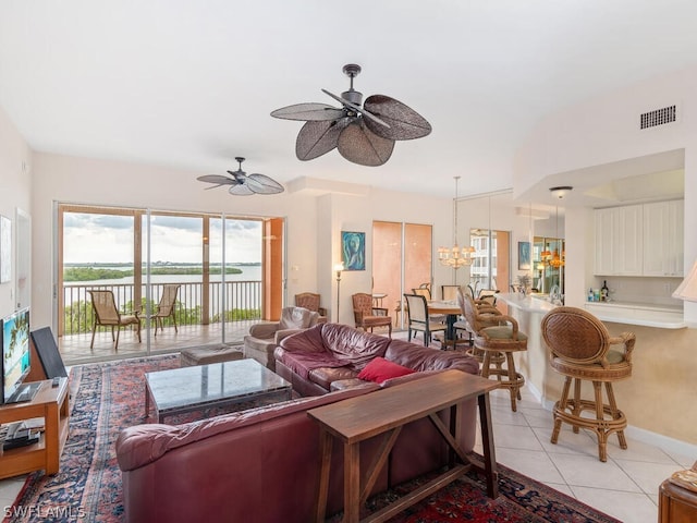 living room featuring ceiling fan with notable chandelier, a water view, and light tile patterned floors