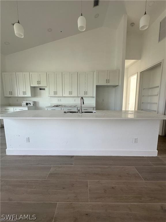 kitchen with white cabinets, decorative light fixtures, and a kitchen island with sink