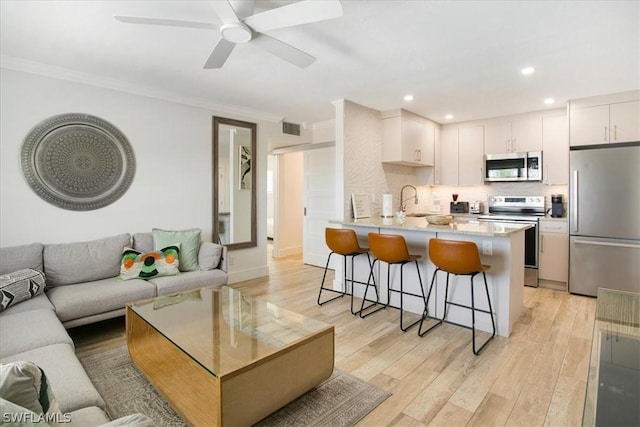 kitchen featuring kitchen peninsula, a kitchen breakfast bar, ornamental molding, stainless steel appliances, and white cabinetry