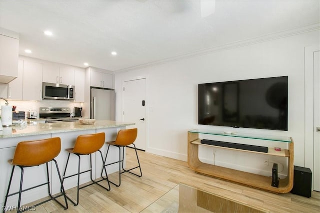 kitchen with appliances with stainless steel finishes, white cabinetry, a kitchen bar, kitchen peninsula, and light wood-type flooring