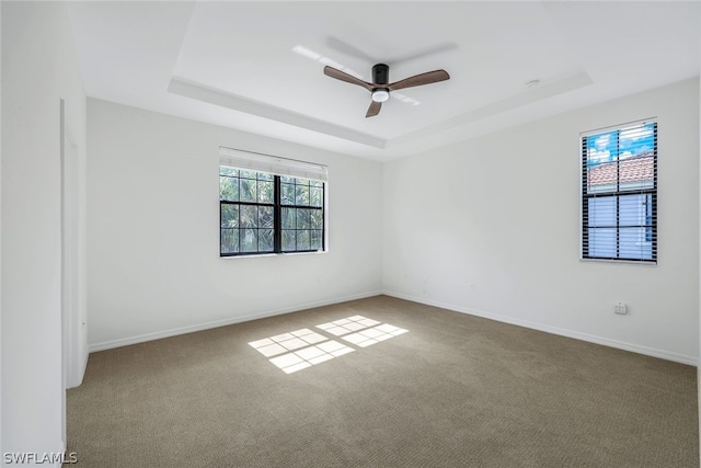 carpeted empty room with a raised ceiling and ceiling fan