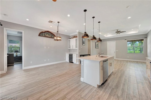 kitchen featuring sink, decorative light fixtures, dishwasher, an island with sink, and a raised ceiling