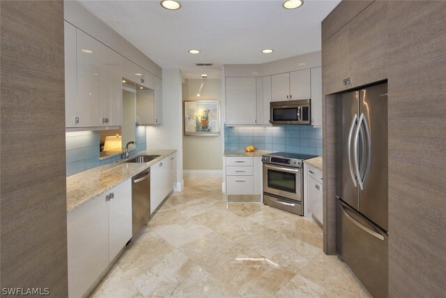 kitchen featuring sink, stainless steel appliances, light stone counters, tasteful backsplash, and white cabinets