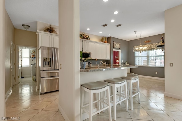 kitchen featuring light tile patterned flooring, a breakfast bar, white cabinets, stainless steel appliances, and hanging light fixtures