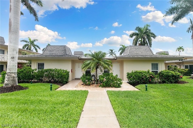 view of front of home with a front yard, mansard roof, and stucco siding