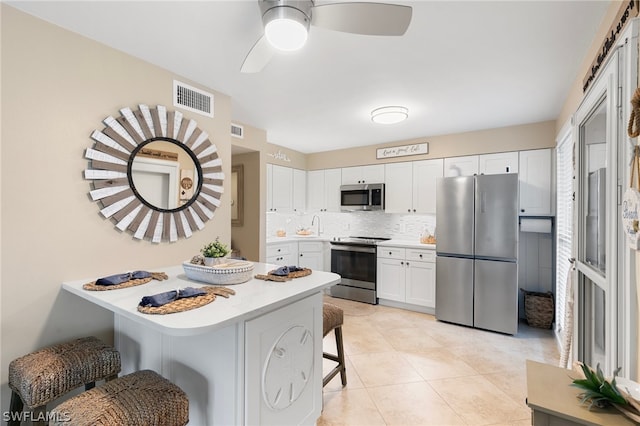 kitchen with ceiling fan, stainless steel appliances, white cabinets, decorative backsplash, and a breakfast bar area