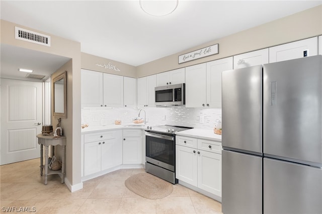 kitchen featuring appliances with stainless steel finishes, light tile patterned floors, tasteful backsplash, and white cabinets