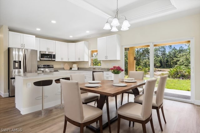 dining room with light hardwood / wood-style flooring, a raised ceiling, a notable chandelier, and crown molding