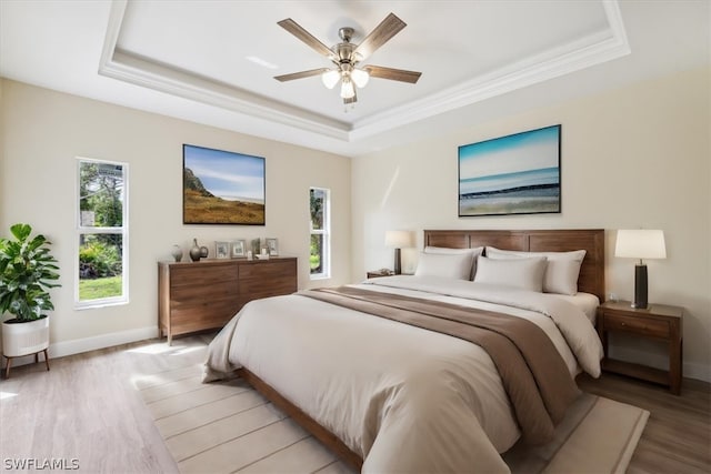 bedroom with light wood-type flooring, a tray ceiling, ceiling fan, and ornamental molding