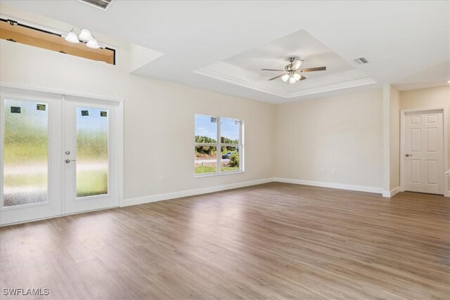 unfurnished room featuring french doors, light hardwood / wood-style floors, a raised ceiling, and ceiling fan