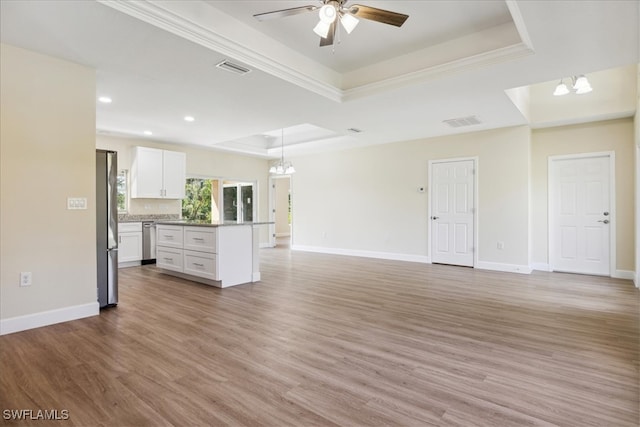 unfurnished living room featuring ceiling fan with notable chandelier, wood-type flooring, crown molding, and a tray ceiling