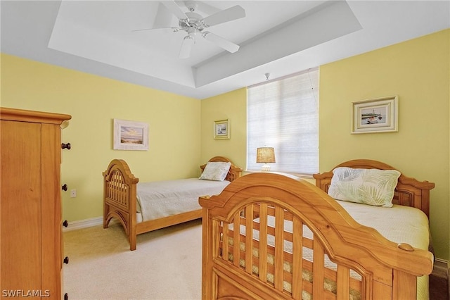 bedroom with ceiling fan, a tray ceiling, and light colored carpet