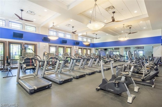 gym with coffered ceiling, ceiling fan, a towering ceiling, and a healthy amount of sunlight