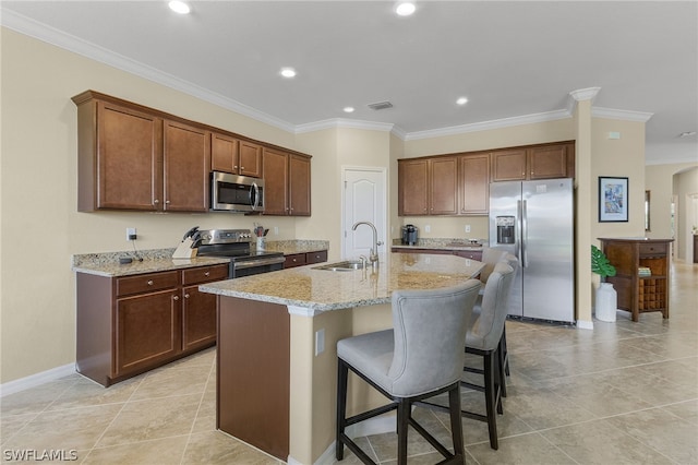 kitchen featuring light stone countertops, ornamental molding, stainless steel appliances, sink, and an island with sink