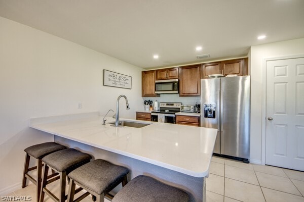 kitchen featuring appliances with stainless steel finishes, sink, kitchen peninsula, light tile patterned floors, and a kitchen breakfast bar