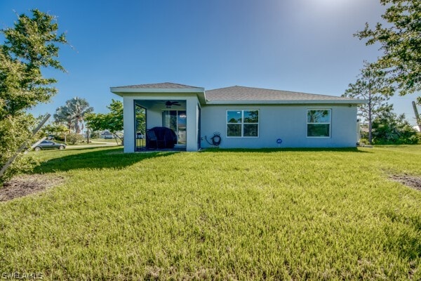 rear view of property featuring ceiling fan and a yard