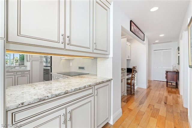 kitchen featuring backsplash, light hardwood / wood-style flooring, black electric stovetop, and light stone countertops