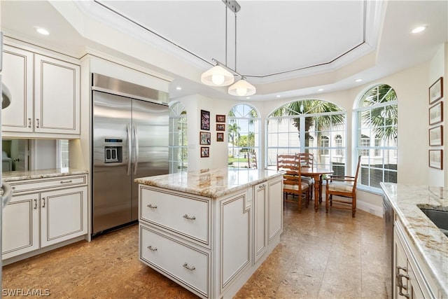 kitchen with pendant lighting, stainless steel built in refrigerator, a raised ceiling, light stone countertops, and a kitchen island