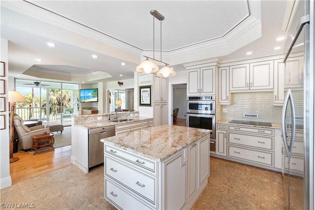 kitchen with pendant lighting, ceiling fan, a raised ceiling, a kitchen island, and stainless steel appliances