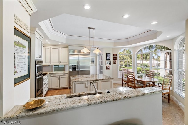 kitchen featuring light stone countertops, appliances with stainless steel finishes, sink, hanging light fixtures, and a raised ceiling