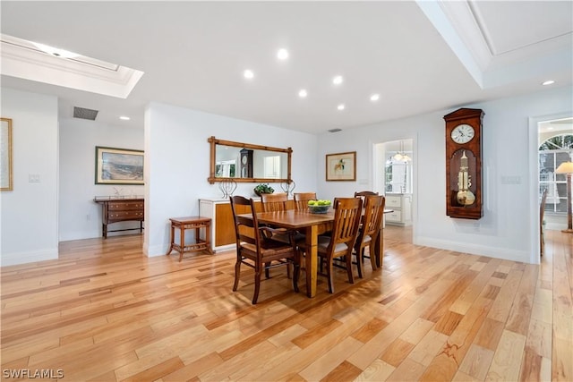 dining room featuring crown molding, a raised ceiling, a skylight, and light wood-type flooring