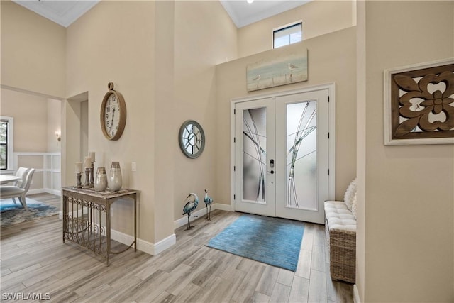 foyer entrance featuring french doors, crown molding, a high ceiling, and light hardwood / wood-style flooring