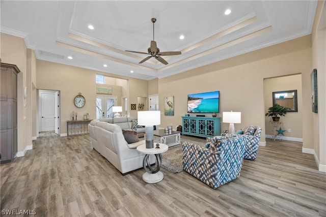 living room featuring a raised ceiling, crown molding, and light wood-type flooring