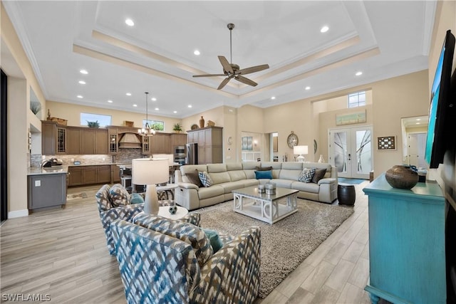 living room with crown molding, ceiling fan with notable chandelier, a raised ceiling, and light wood-type flooring